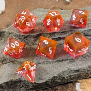May include: A set of seven polyhedral dice for tabletop games. The dice are made of translucent orange resin with white numbering. The dice are arranged on a gray stone surface.