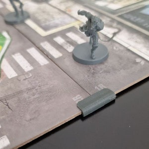 May include: A close-up of a grey plastic game board with a grey plastic figure standing on a grey plastic base. The figure is in a fighting pose with its arms raised. The board has a white and grey striped pattern.