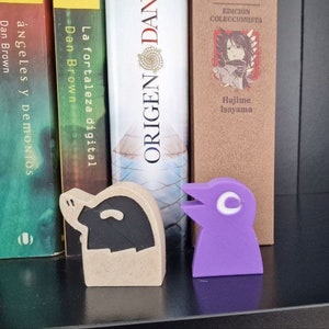 May include: Two small figurines on a bookshelf. The figurine on the left is a brown and black pig. The figurine on the right is a purple bird with a white eye.