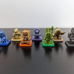 May include: Eight miniature figurines painted in different colors, each standing on a small base. The figurines are a variety of characters, including a cat, a robot, a knight, and a creature with wings.