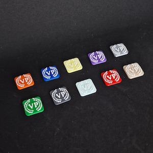 May include: Twelve square game pieces with a white wreath and the letters "VP" inside. The pieces are in different colors: orange, green, gray, light blue, yellow, purple, beige, red, and white.