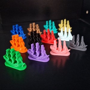 Op de afbeelding: Een set van 12 miniatuur schepen in verschillende kleuren, waaronder rood, oranje, geel, groen, blauw, paars, zwart en wit. De schepen zijn gemaakt van plastic en hebben een gedetailleerd ontwerp.