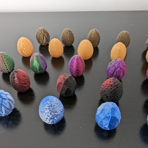 Può includere: Una collezione di 20 uova in ceramica colorate, con motivi e trame intricate. Le uova sono disposte a semicerchio su una superficie scura. Le uova sono di vari colori, tra cui blu, verde, viola, rosso e marrone.