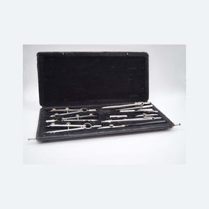 May include: A vintage drafting set in a black case. The set includes several silver-colored compasses, dividers, and other drawing tools. The case is open, revealing the tools neatly arranged on a black velvet-like interior.