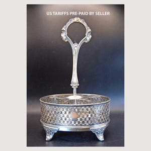 Peut inclure: Plat de service argenté avec une poignée décorative et un motif ajouré. Le plat a une base ronde soutenue par des pieds ornés. Le texte "US TARIFFS PRE-PAID BY SELLER" est visible en haut.