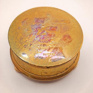 May include: A circular, gold-coloured trinket box with a textured surface and small feet. The lid displays a map of Scotland with city names including Glasgow and Edinburgh. The box has a vintage appearance.