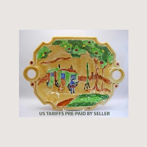 Könnte beinhalten: Dekorative Keramik-Servierplatte mit handgemalter Szene eines Dorfes mit einem Eisenbahnwagen, Bäumen und einer Figur mit Gewehr. Die Platte hat einen gelben Rand mit roten Akzenten und zwei kreisförmigen Griffen. Der Text "US TARIFFS PRE-PAID BY SELLER" ist unten aufgedruckt.
