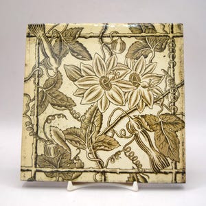 Può includere: Una piastrella in ceramica quadrata con una stampa botanica marrone scuro su sfondo color crema. Il design mostra due grandi fiori della passione circondati da intricati motivi a viticcio, foglie seghettate e piccoli boccioli rotondi.