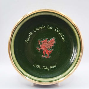 May include: A green ceramic plate with a gold rim. The plate features the text "Penarth Classic Car Exhibition" and "24th July 1974". A red dragon emblem is in the center.
