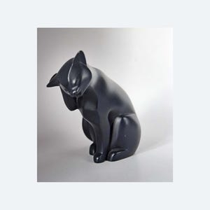May include: A black cat ornament in a seated pose, grooming its paw. The sculpture has a smooth, matte finish and is set against a white backdrop. The cat's ears are pricked, and its body is slightly curved.