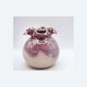 Op de afbeelding: Een handgemaakte keramische vaas met een ronde body en een gerimpelde rand. De vaas heeft een tweekleurig ontwerp, met een diepe bordeauxrode kleur op het bovenste gedeelte en een lichtere, gespikkelde beige op de onderste helft. De vaas is ongeveer 15 cm hoog.