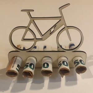 Può includere: Porta soldi in legno a forma di bicicletta con cinque banconote da 50 euro arrotolate inserite nelle fessure.