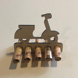 Puede incluir: Corte de madera de una scooter con cinco billetes enrollados insertados en las ranuras. Los billetes son euros.