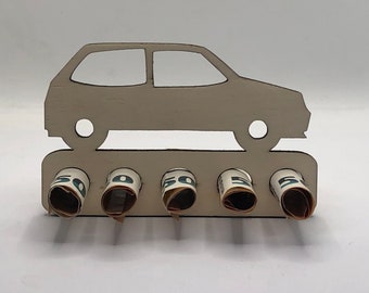 Könnte beinhalten: Holz-Geldhalter in Form eines Autos mit fünf Schlitzen für gerollte Geldscheine. Das Auto ist weiß lackiert und hat ein ausgeschnittenes Design.