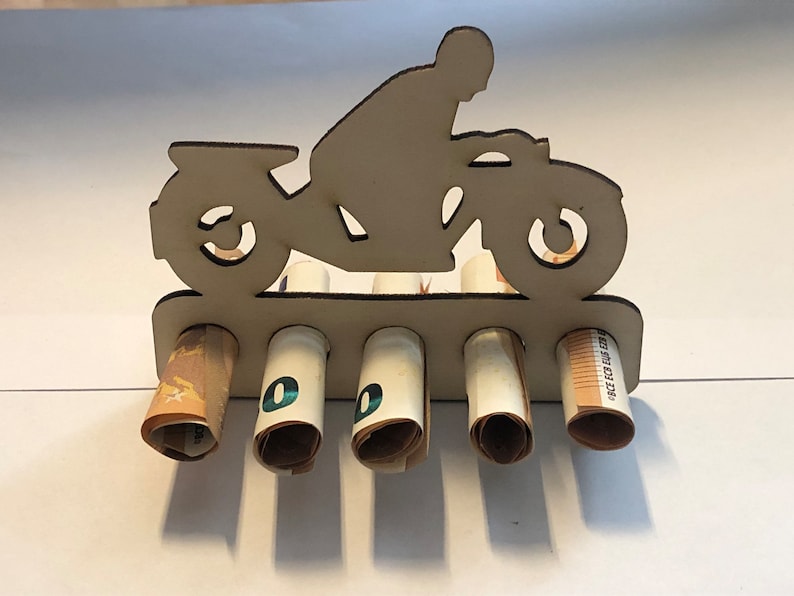 Peut inclure: Porte-monnaie en bois en forme de moto avec cinq fentes pour billets roul&eacute;s. La moto est peinte en brun et a une silhouette de pilote.