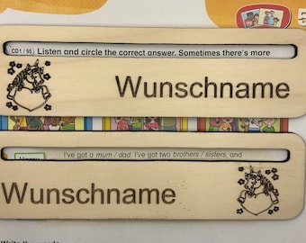 May include: Two wooden name tags featuring a unicorn design and the text "Wunschname" on each. The top tag has the text "CD1/55 Listen and circle the correct answer. Sometimes there's more" on it. The bottom tag has the text "I've got a mum/dad. I've got two brothers/sisters, and" on it.