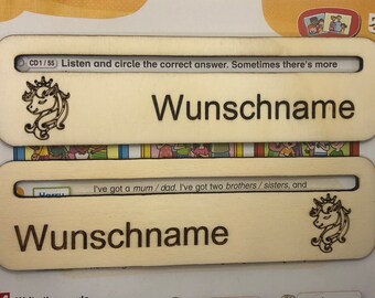 May include: Two wooden name tags featuring a unicorn design and the text "Wunschname". The top tag includes the text "CD1/55 Listen and circle the correct answer. Sometimes there's more". The bottom tag has the text "I've got a mum/dad. I've got two brothers/sisters, and".
