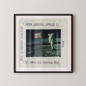 May include: A framed photographic slide of the Apollo 11 moon landing featuring an astronaut standing near an American flag. The slide mount includes the text MOON LANDING—APOLLO 11, MFG. by HOLIDAY FILM CORP., 40-55, and 17. Aldrin and American Flag.