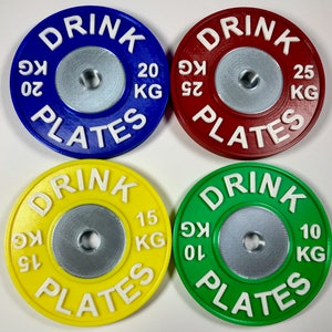 Könnte beinhalten: Vier Gewichtsplatten mit dem aufgedruckten Text "DRINK PLATES". Die Platten sind in den Farben Blau, Rot, Gelb und Grün gehalten. Die Platten sind mit den Gewichten 20 kg, 25 kg, 15 kg und 10 kg beschriftet.