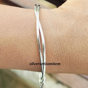 May include: A silver bangle bracelet with a twisted design. The bracelet is made of two strands of silver that are intertwined.