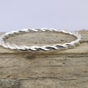 Può includere: Un anello a fascia ritorta in argento. L'anello è sottile e delicato, con una finitura liscia e lucida.