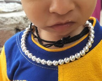 May include: A silver beaded necklace with a black cord closure. The necklace is worn over a blue and yellow shirt.