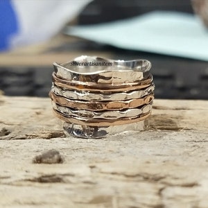 May include: A silver and copper spinning ring with a hammered texture. The ring is made of multiple bands that spin around each other.