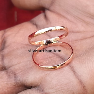May include: Two thin gold-colored rings, one stacked on top of the other, on a person's hand.