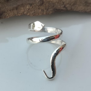 Op de afbeelding: Zilverkleurige ring in een slangenontwerp. De ring wikkelt zich om de vinger met een gehamerde afwerking. De slangenkop heeft een ruitvormig detail en de staart buigt omhoog.