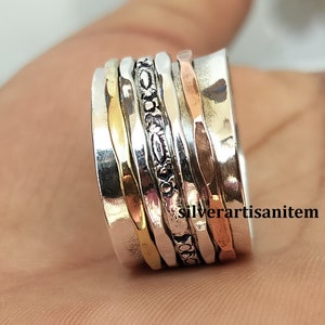 May include: A silver, gold, and copper spinning ring with a decorative pattern. The ring is made of multiple bands that spin around each other.