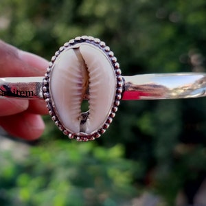 Op de afbeelding: Zilveren armband met een witte kauri schelp in het midden. De schelp is omgeven door een parelrand.