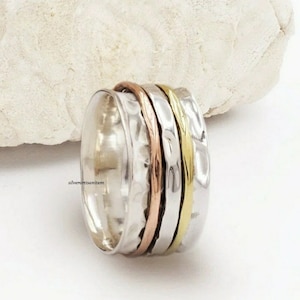 May include: A silver spinning ring with three bands of gold, copper, and silver. The ring is hammered and has a textured surface.