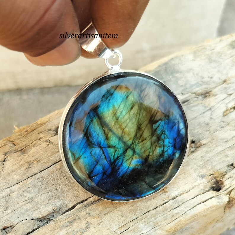 May include: A round pendant with a polished, iridescent labradorite stone set in a silver bezel. The stone displays a vibrant play of color, with blues, greens, and yellows. The pendant has a silver bail for a chain.