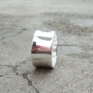 May include: A wide silver band ring with a smooth, polished finish. The ring is made of sterling silver and has a simple, modern design.
