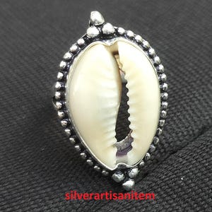 Op de afbeelding: Een zilveren ring met een witte kauri schelp in het midden. De ring is versierd met kleine zilveren kralen rond de rand.