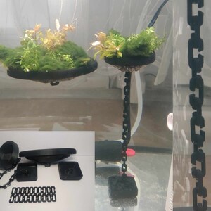 May include: Two black hanging planters with chains. The planters are filled with green plants and are suspended from the ceiling. The planters are made of a hard plastic material.
