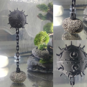 May include: A black and grey decorative nautical-themed ornament with a chain. The ornament is shaped like a round bomb with spikes and is hanging from a chain.