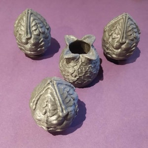 May include: Four 3D printed silver-coloured alien eggs, three are closed and one is open with a textured interior.