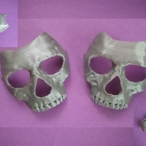 May include: Two white 3D printed skull masks with eye and nose holes. The masks are on a purple background.