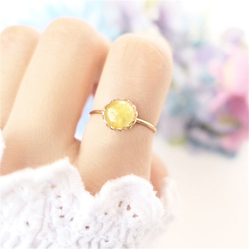 Pode incluir: Um anel de ouro com uma pedra redonda amarela com borda festonada.
