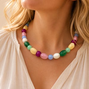 May include: A necklace featuring a series of smooth, polished beads in various colours including yellow, purple, pink, light blue, white, and green. The beads are rounded and oval-shaped, strung together to form a vibrant, multi-coloured accessory.