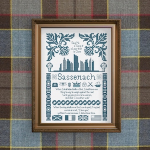 Peut inclure: Un cadre contenant une broderie au point de croix avec du fil bleu foncé sur fond blanc. Le motif inclut le texte "Sassenach", une silhouette de ligne d'horizon, des motifs floraux et diverses citations. Le cadre est brun moyen avec un bord décoratif.