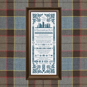 Peut inclure: Une œuvre d'art encadrée en point de croix avec un cadre en bois foncé. L'œuvre présente du texte bleu et des éléments décoratifs sur un fond blanc. Le texte comprend le mot "Sassenach". Le fond est un motif à carreaux.
