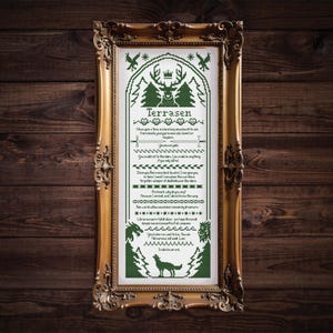 May include: A framed cross-stitch artwork in a gold ornate frame. The artwork features the word "Terrasen" at the top, with decorative elements including a deer, trees, and a wolf. The text is in green on a white background.