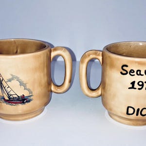 May include: A white ceramic mug with a black handle and the text "But First, Coffee" in a black, handwritten-style font. The mug is on a white surface.