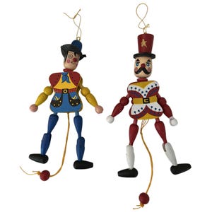 May include: Two wooden marionette figures. One is a clown with a blue hat and outfit, the other is a soldier with a red top hat and uniform. Both have articulated limbs and are painted in bright colors.