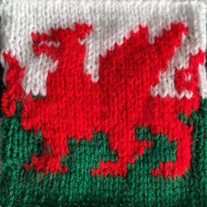 May include: A knitted Welsh flag with a red dragon on a white background and a green background.
