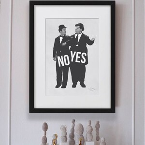 Puede incluir: Fotograf&iacute;a en blanco y negro de dos hombres con traje y sombrero sosteniendo un cartel que dice "NO YES". La fotograf&iacute;a est&aacute; enmarcada en un marco negro y est&aacute; colgada en una pared blanca. Hay varias peque&ntilde;as esculturas redondas grises sobre una superficie blanca debajo del marco.