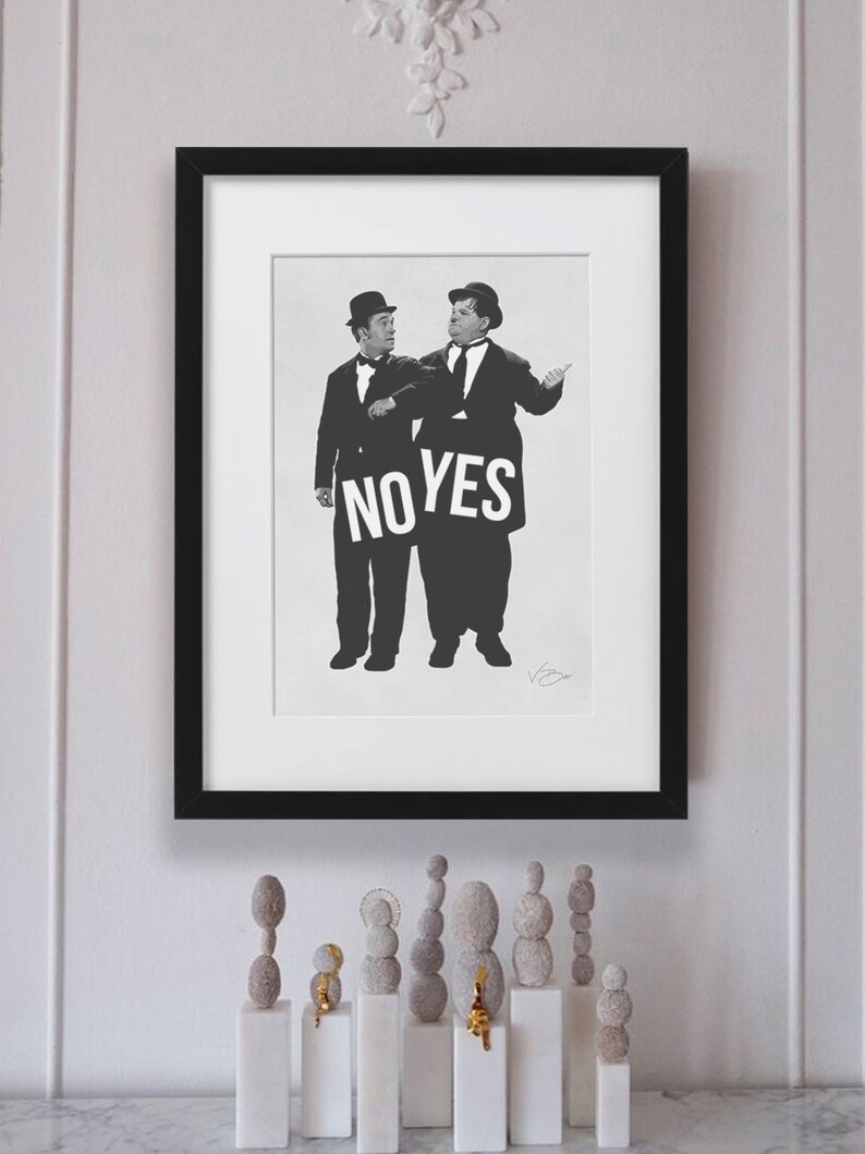 Puede incluir: Fotograf&iacute;a en blanco y negro de dos hombres con traje y sombrero sosteniendo un cartel que dice "NO YES". La fotograf&iacute;a est&aacute; enmarcada en un marco negro y est&aacute; colgada en una pared blanca. Hay varias peque&ntilde;as esculturas redondas grises sobre una superficie blanca debajo del marco.