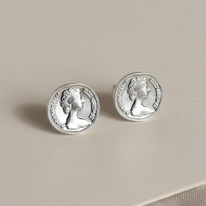 May include: A pair of silver-toned stud earrings. Each earring features a detailed profile of a person within a circular frame. The earrings have a vintage or antique aesthetic, with a slightly tarnished appearance.